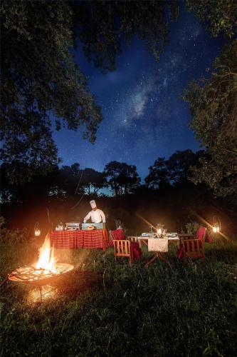 a man sitting at a table around a fire at night at Olare Mara Kempinski in Talek