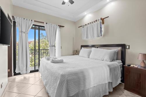 a bedroom with a bed with white sheets and a window at The Oaks Tamarindo Pool Front Condominiums fast wifi in Tamarindo