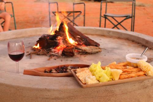 a fire pit with a plate of food and a glass of wine at Orpheus Inn Camping in Kaneb Pos