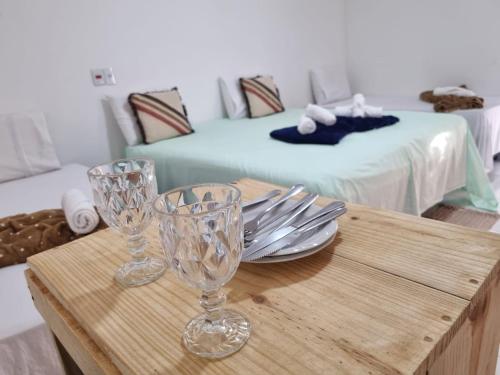 two wine glasses on a wooden table with a bed at Pousada Jardim da Lagoa-BA in Bom Jesus da Lapa