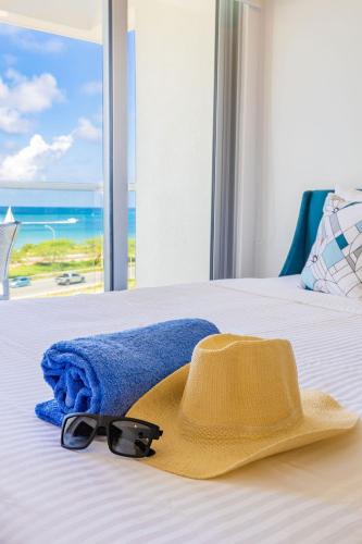 a yellow hat and a towel and sunglasses on a bed at Azure Beach Residences in Palm-Eagle Beach