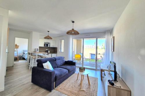 un salon avec un canapé bleu et une cuisine dans l'établissement Bright apartment with balcony and garden, à Saint-Coulomb