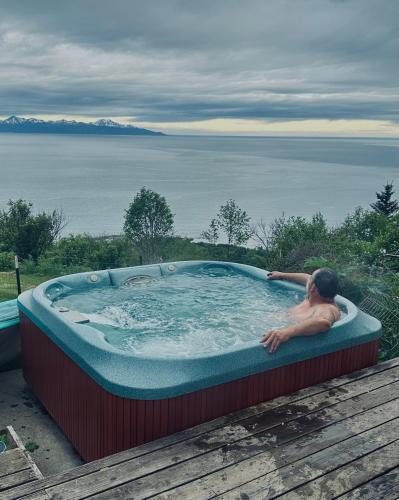 a man in a jacuzzi tub with a view of the water at Paradise Suites Eagles Nest in Homer