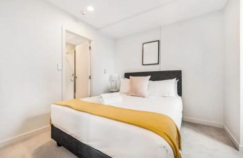 a white bedroom with a large bed with a yellow blanket at Just opposite to Skytower, 2 Bed 2 Bath in CBD in Auckland