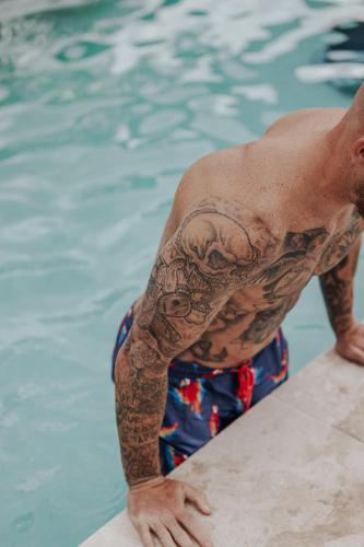 a man with tattoos on his arm in a swimming pool at The Wellness Farm Broke in Broke