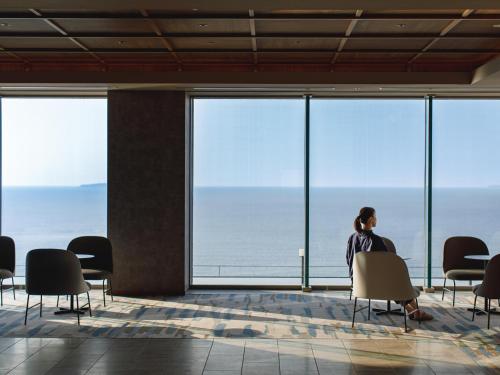 a woman sitting on a chair looking out at the ocean at Atami Izusan Karaku in Atami