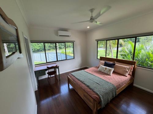 a bedroom with a bed and a table and windows at Jabiru Stay Daintree Village in Daintree
