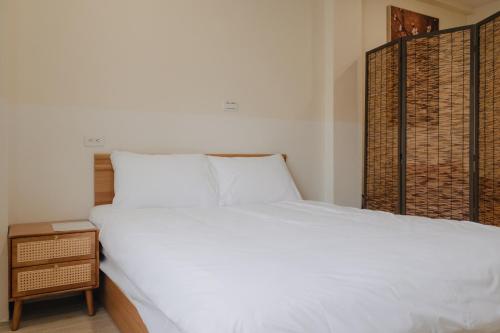 a bedroom with a large white bed and a night stand at Boléro Homestay I 鄰近花園夜市 in Tainan