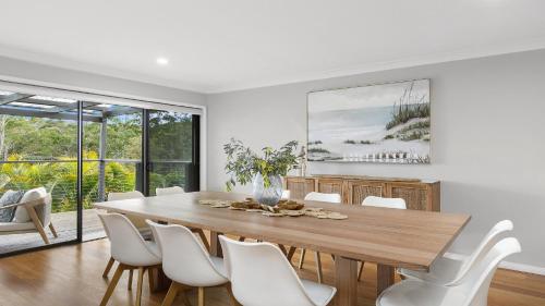 a dining room with a wooden table and white chairs at 'Bay Dreams at Killcare' by HolidayCo in Killcare