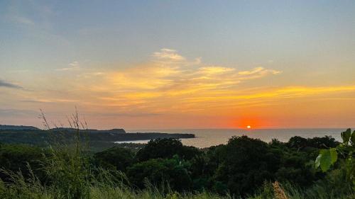 a sunset over a body of water with trees at MARACUYA at Limoncito Beach in Limoncito Hill
