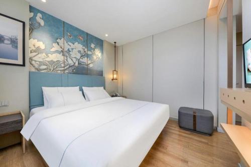 a large white bed in a room with a painting at Magnotel Hotel Xiamen North Station Binhai in Xiamen