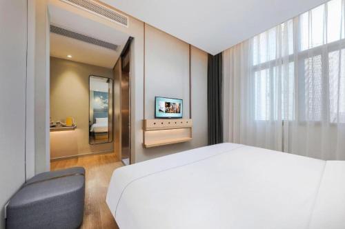 a bedroom with a bed and a chair and a mirror at Magnotel Hotel Xiamen North Station Binhai in Xiamen