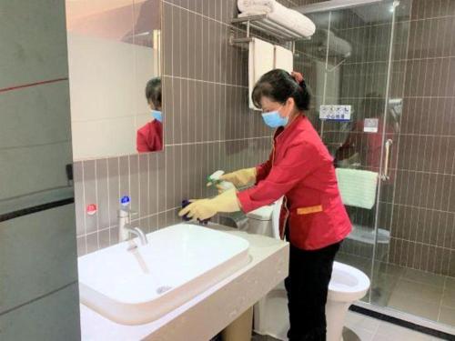 a woman wearing a mask washing a sink in a bathroom at Thank Inn Plus Hotel Guangdong Yunfu Luoding City Municipal in Yunfu