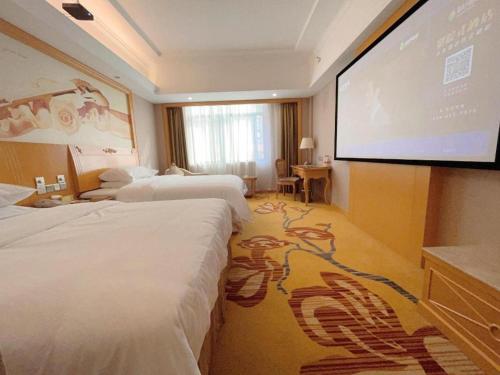 a hotel room with three beds and a projection screen at Vienna Hotel Guangxi Fangcheng in Fangcheng