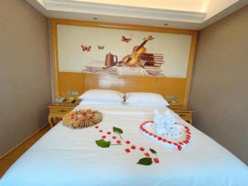 a bedroom with a white bed with a picture of a violin at Vienna Hotel Guangxi Fangcheng in Fangcheng