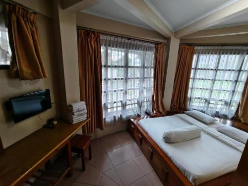 a bedroom with two beds and a tv and windows at Sapadia Hotel Parapat in Parapat