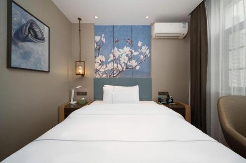 a bedroom with a large white bed and a painting at Magnotel Changsha Wuyi Square Metro Station National Finacial Center in Changsha