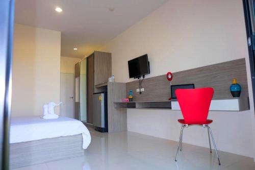 a red chair in a room with a bed and a tv at The Pride in Nakhon Pathom