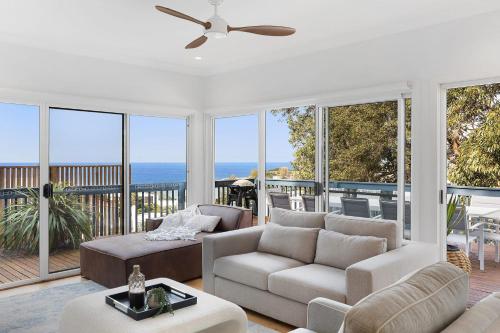 a living room with white furniture and large windows at Barnhill Beach House - by Coast Hosting in Terrigal