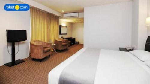 a hotel room with a bed and chairs and a tv at Kenari Tower Hotel in Makassar