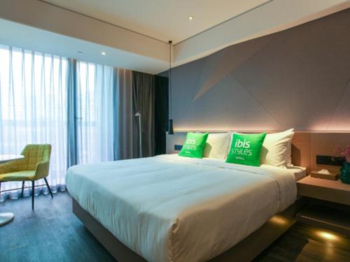 a hotel room with a large bed with green pillows at ibis Styles Yangzhou Baixiang Rd Hotel in Yangzhou