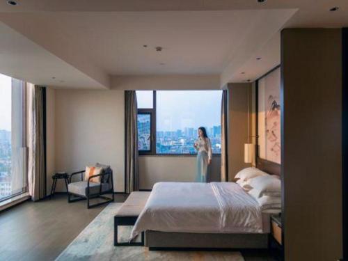 a woman standing in a bedroom with a large bed at Dajiuhua Hotel in Chizhou