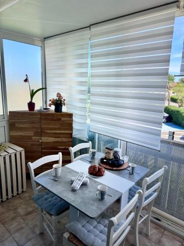 une salle à manger avec une table et une fenêtre avec des stores dans l'établissement Le Scarlett- Confort à Palavas-Plage à proximité, Terrasse, Piscine et Clim -LaConciergerieByNina, à Palavas-les-Flots