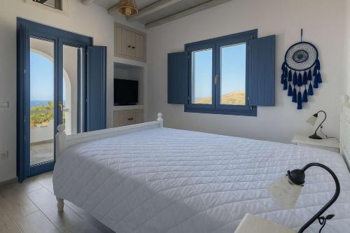 a bedroom with a large white bed with blue windows at Folegandros Enchanting Moniasma Home, Sunset Views in Ano Meria