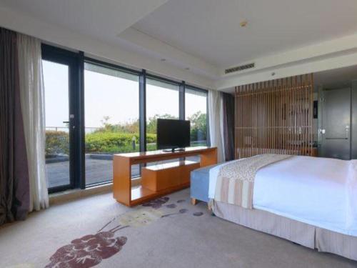 a bedroom with a bed and a tv and large windows at Suzhou Qingshan Conference Center in Suzhou