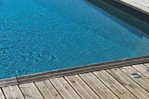 une piscine d'eau bleue à côté d'une terrasse en bois dans l'établissement Maison à la campagne avec piscine chauffée proche Deauville, à Saint-Étienne-la-Thillaye