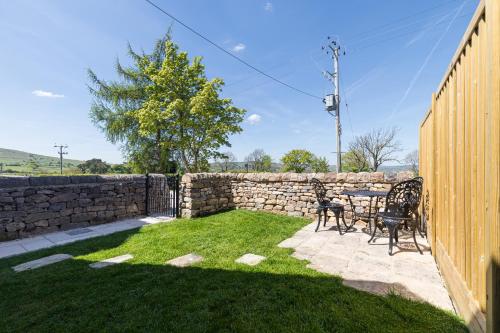 a patio with a table and chairs next to a stone wall at Country Cottage with Hot Tub - pre-heated for your arrival in Buxton