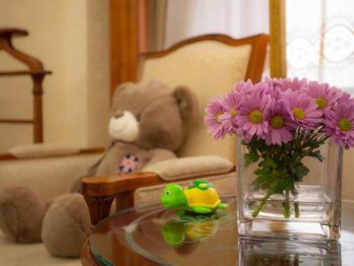 a vase with purple flowers in front of a teddy bear at Quanzhou Hotel in Quanzhou