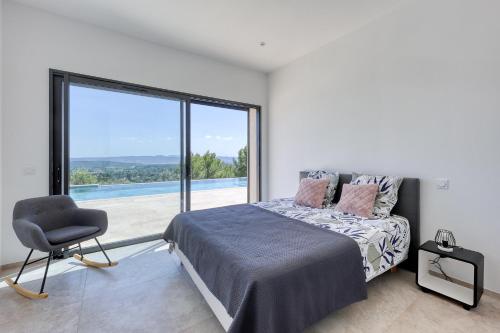 a bedroom with a bed and a chair and a large window at Bella Vista Cotignac - Piscine Privée in Cotignac