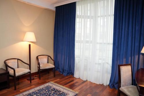a room with two chairs and a window with blue curtains at Taj Palace Hotel in Dushanbe