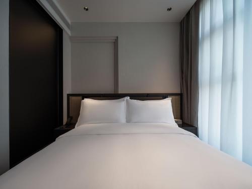 a bed with white sheets and a large window at 中濠悦际酒店 深圳国际会展中心店 in Shenzhen