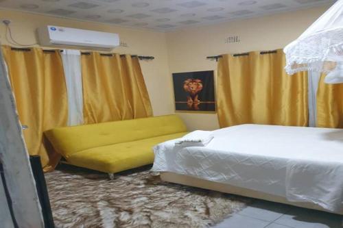 a bedroom with a bed and a yellow couch at Glamour Lodges and Apartments in Livingstone