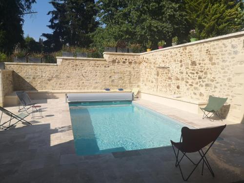 une piscine avec des chaises et un mur en pierre dans l'établissement Les Ombelles, à Saint-Estèphe