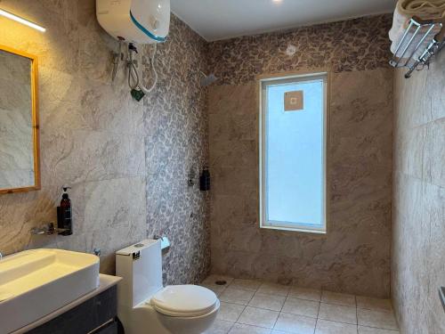 a bathroom with a toilet and a sink and a window at Whispering Oaks by Happy Himalayan in Rāmgarh