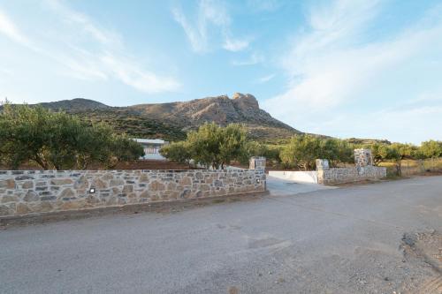 a road with a stone wall with a mountain in the background at Chryselia Suites- Private Pool in Keratokampos