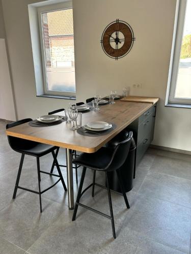 a dining room table with chairs and a clock on the wall at Les gîtes de la ferme du moulin in Binche