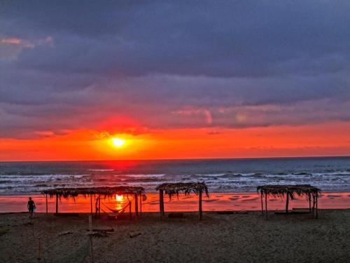 a sunset on the beach with a person walking on the beach at Sundown Beach Hotel in Canoa