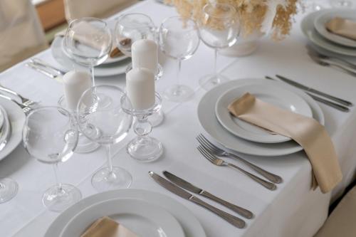 a white table with wine glasses and plates and silverware at Hotel Pušyno Namai in Tirkšliai
