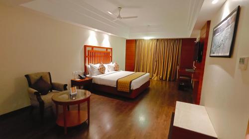 a hotel room with a bed and a chair and a table at MM Legacy - A Bergamont Hotel, Kanchipuram in Kanchipuram