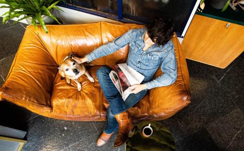 a woman sitting on a couch reading a book with a dog at Hobo Hotel Stockholm in Stockholm