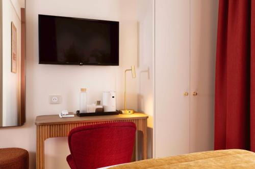 a room with a desk with a red chair and a tv at Hôtel Le Cardinal in Paris