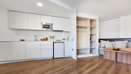 a kitchen with white cabinets and a couch in the background at Flacalco Hotel & Apartments in Cala Ratjada