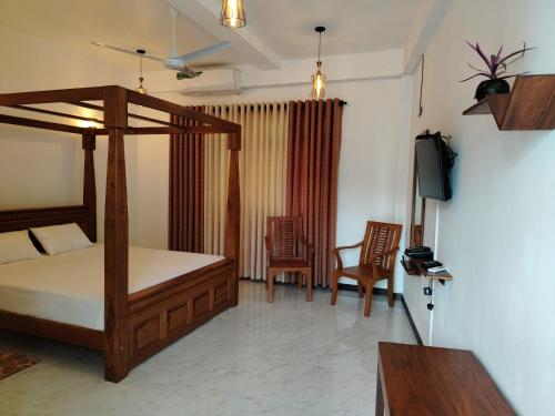a bedroom with a bed and two chairs and a television at Diora Hotel in Ratnapura