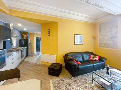 a living room with a leather couch and a kitchen at Résidence Verdi - Appartements meublés en centre ville in Bédarieux