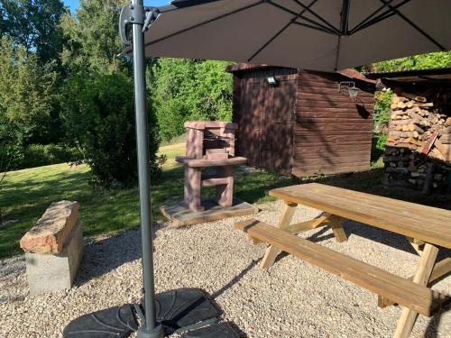 a picnic table with an umbrella and a wooden bench at Chalet et jacuzzi au coeur du Nivernais in Sauvages