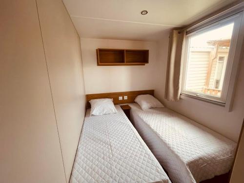 deux lits dans une petite pièce avec une fenêtre dans l'établissement Mobil Home Bouginvilliers 5, à Valras-Plage